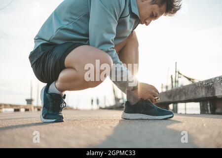 gros plan sur l'homme qui noue les lacets de chaussures sur la route avant de courir au coucher du soleil. Sport et entraînement. Banque D'Images