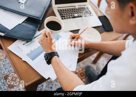 homme d'affaires tenant une tasse de café dans les mains et ordinateur sur table dans le café. Un jeune travailleur indépendant boit du café et travaille. Banque D'Images