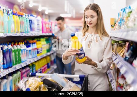 Portrait d'une jeune femme avec un chariot à provisions choisissant des produits chimiques domestiques dans un supermarché Banque D'Images