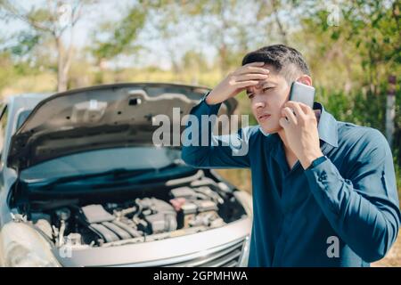 jeune homme appelant, envoyant un sms pour un service de voiture sur l'assistance routière après la voiture brisée. Voiture cassée, concept de panne de voiture. Banque D'Images