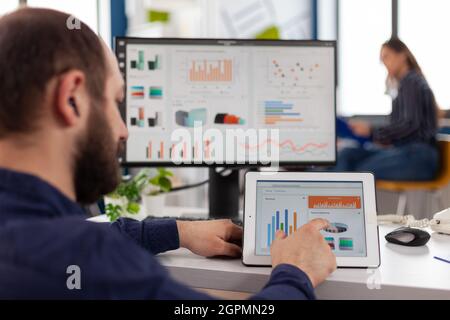 Homme d'affaires en fauteuil roulant analysant le graphique financier à l'aide d'une tablette informatique travaillant à la gestion des statistiques dans le bureau de la société de démarrage. Manager handicapés planifiant une stratégie numérique Banque D'Images