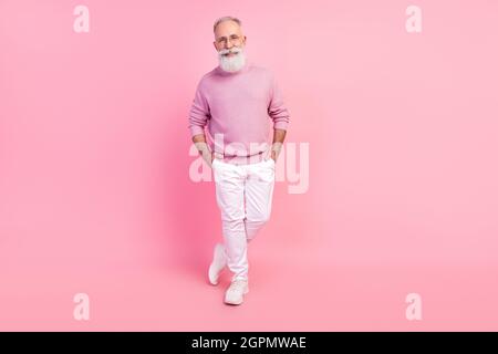 Photo de charmant homme mûr habillé pull-over verres souriant bras de marche poches isolé couleur rose fond Banque D'Images