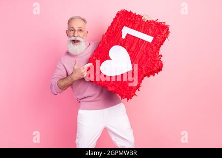 Photo de impressionné joli âge gentleman porter des lunettes de chandail pointant le doigt coeur comme signe sourire isolé couleur rose fond Banque D'Images