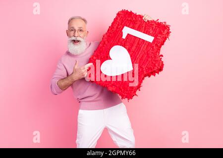 Photo de impressionné joli âge gentleman porter des lunettes de chandail pointant le doigt coeur comme signe sourire isolé couleur rose fond Banque D'Images
