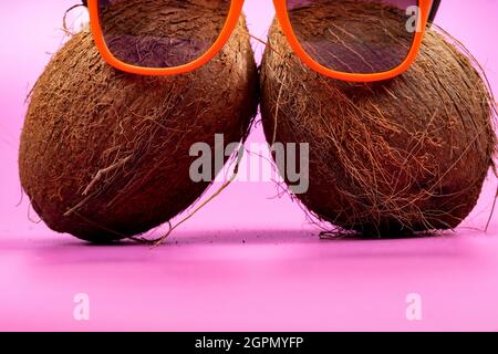 Deux noix de coco entières et des verres d'orange sur fond rose. Banque D'Images