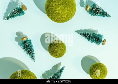 Jouets arbres de noël et boules d'herbe vertes dispersées sur fond bleu. Motif conceptuel avec ombres dures. Banque D'Images