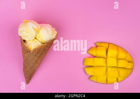 Boules de crème glacée au mangue dans un cône de gaufres sur fond rose. Mangue mûre avec glace sur fond rose Banque D'Images