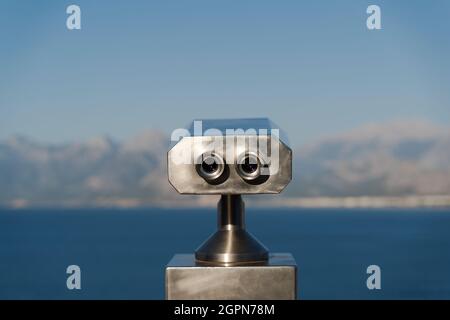 vue arrière gros plan de jumelles en aluminium à pièces avec vue panoramique sur la mer et les montagnes en arrière-plan Banque D'Images