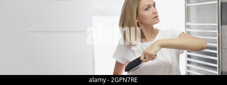 Femme peignant ses cheveux avec peigne dans la salle de bains devant le miroir Banque D'Images