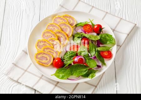 jambon et fromage hachés petits-déjeuners omelettes, pignons et salade d'oignons rouges aux tomates fraîches aux épinards sur une assiette sur une table en bois blanc, horizontale v Banque D'Images