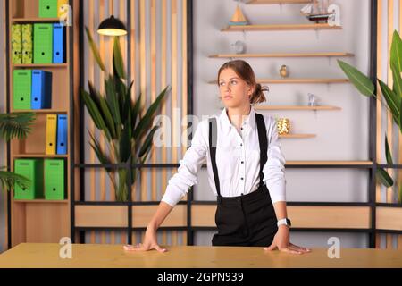 Jeune fille belle dans le style de bureau regarde l'appareil photo. Un adolescent dans les vêtements de l'école dans le bureau. Jeune enseignant dans une classe scolaire. Fille d'affaires au bureau Banque D'Images