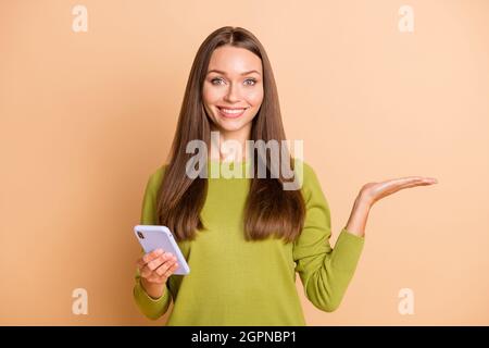 Portrait d'une jolie fille gaie utilisant un gadget tenant sur la paume de la copie espace publicité isolée sur fond beige couleur pastel Banque D'Images