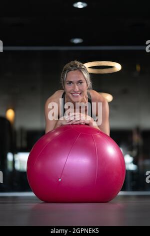 Jeune femme blonde s'exerçant dans une salle de gym avec une grosse balle rose Banque D'Images