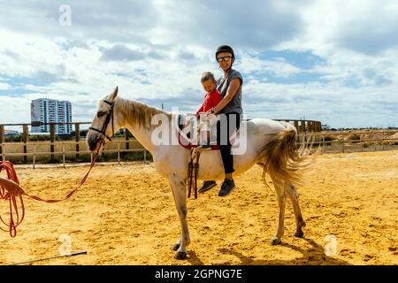 Une femme avec son fils de 3 ans assise sur le cheval dans un enclos Banque D'Images