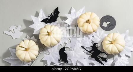 Concept Halloween. Feuilles d'érable blanc fantôme sur une branche et citrouilles blanches. Décor traditionnel de vacances sur fond gris. Une lumière dure et sombre tendance Banque D'Images