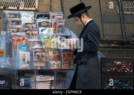 Un jeune hassidique lit un périodique d'un porte-revues avec des titres hébraïques, yiddish et anglais. À Williamsburg, Brooklyn, New York. Banque D'Images