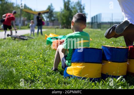 Le garçon est assis sur l'aire de jeux. Un enfant sur un pouf doux. Enfant en été dans la rue. Le garçon est fatigué de jouer. Banque D'Images