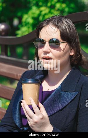 Une jeune femme tient une tasse de papier de café et une paille pour boire. Banque D'Images