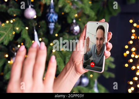 La main de la femme fait un message d'accueil sur l'écran du smartphone sur le fond d'un arbre de Noël. Concept de message d'accueil en ligne. Coronavirus et quaran Banque D'Images