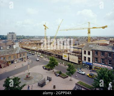 Vue du nord-est sur la place du marché de Carlisle vers le site de construction du centre commercial Lanes, montrant les grues Laing contre la ligne d'horizon. Le contrat pour le centre commercial Lanes a été attribué à John Laing Construction, Division du Nord en octobre 1982, et sa construction a pris environ deux ans. La configuration de type H du complexe a été construite dans des cadres en béton armé sur des chapeaux de pieux et des poutres de sol, avec une grande zone de sous-sol à l'extrémité inférieure du site. Le complexe comprenait quatre grands magasins, 50 unités commerciales plus petites, une bibliothèque de comté à trois niveaux, 27 unités de logement Banque D'Images