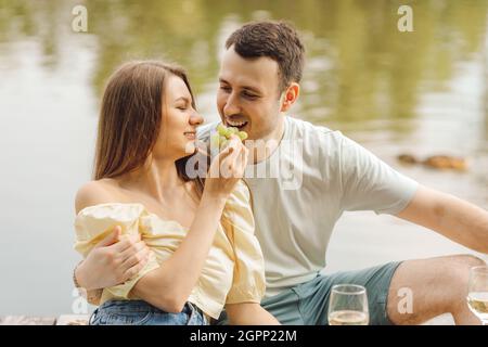 L'homme encadre sa petite amie, et elle lui nourrit des raisins pendant un pique-nique romantique dans la nature. Bonheur et sérénité. Repos et plaisir. Super jour. Romantique RE Banque D'Images