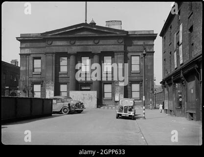 Hôtel de ville, place Bexley, Salford, 1942. Vue extérieure de l'hôtel de ville, montrant la façade sud avec deux voitures contemporaines au premier plan. Le hall a été construit par Richard Lane entre 1825 et 1827, et la façade sud a deux étages et cinq baies, avec un portique de trois baies Doric avec des colonnes géantes, un fronton et une frise avec quatre couronnes de relief. Sur l'image, les fenêtres sont en tissu d'obscurcissement et un mur de briques temporaire recouvre l'entrée principale. Le mobilier de rue est peint avec des bandes noires et blanches, pour faciliter la conduite nocturne pendant la Seconde Guerre mondiale Banque D'Images