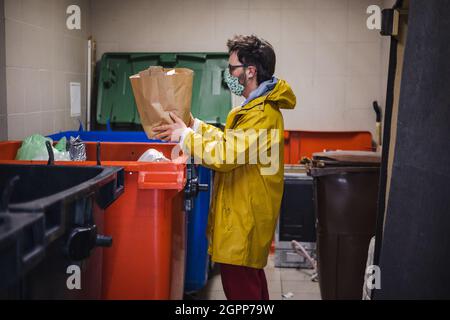 Un homme portant un masque pour le visage jette des déchets dans un conteneur Banque D'Images