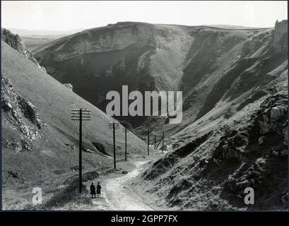 Col Winnats, Castleton, High Peak, Derbyshire, années 1930. Un couple debout à la tête de Winnats Pass. Au début des années 1930, Winnats Pass a été le site d'un rassemblement, auquel ont participé 10,000 personnes, pour faire campagne pour l'accès aux landes et autres campagnes ouvertes. À peu près à la même époque, une intrusion massive de Kinder Scout, à proximité, par des randonneurs et des membres de la Ligue des jeunes communistes, a eu lieu. Cet acte de désobéissance civile s'est produit à peine 5 mois avant l'adoption de la « loi sur les droits de passage » en 1932 et a sans doute contribué à ouvrir la voie à l'établissement du premier National Trail de Grande-Bretagne, le Pennine Way long dis Banque D'Images