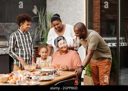 Portrait d'une femme âgée heureuse célébrant son anniversaire en famille et bougies soufflantes sur le gâteau d'anniversaire Banque D'Images