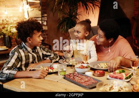 Portrait aux tons chaleureux d'une famille afro-américaine heureuse qui apprécie le dîner en plein air en mettant l'accent sur les enfants souriants et la grand-mère aimante Banque D'Images