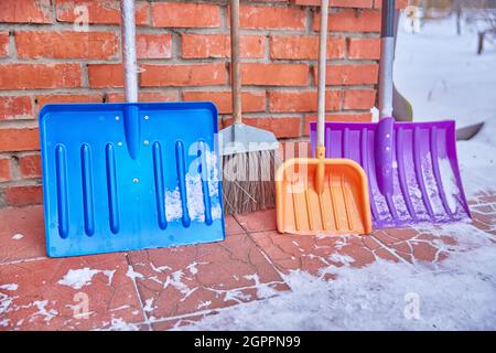 Des pelles à neige en plastique coloré se tiennent près du mur de briques de la maison concept familial de nettoyage de la maison et de la zone autour de la maison Banque D'Images