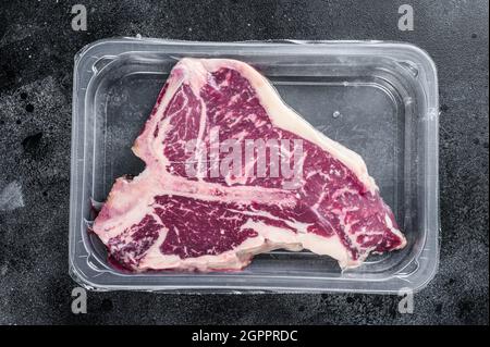 T-bon steak de bœuf cru dans un emballage sous vide. Arrière-plan noir. Vue de dessus Banque D'Images