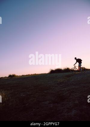 Vélo de montagne solitaire rétro-éclairé en fin de soirée paysage herbeux et ciel - vélo tout-terrain - espace de copie - paysage cycliste solitaire Banque D'Images