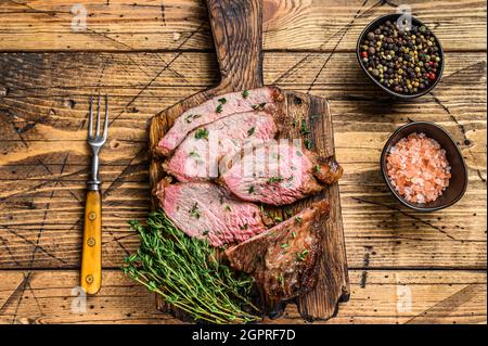 Tranches rares de rôti de boeuf sirloin à trois pointes steak bbq sur une planche à découper en bois. fond en bois. Vue de dessus Banque D'Images