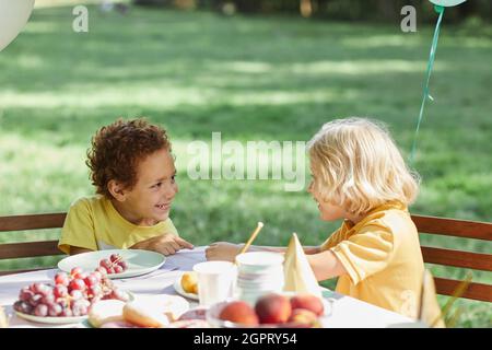 Deux petits enfants à la table de pique-nique à l'extérieur, décorés de ballons pour la fête d'anniversaire en été, espace copie Banque D'Images