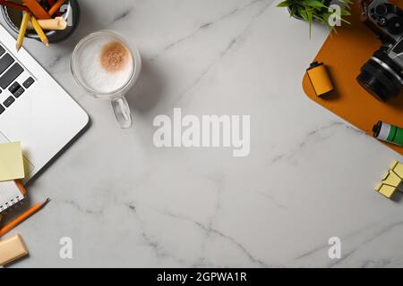 Tasse de café, ordinateur portable et appareil photo sur table en marbre. Banque D'Images