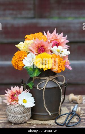 bouquet rustique de fleurs de tagetes et de zinnia jaune et orange dans une laitette millésime Banque D'Images