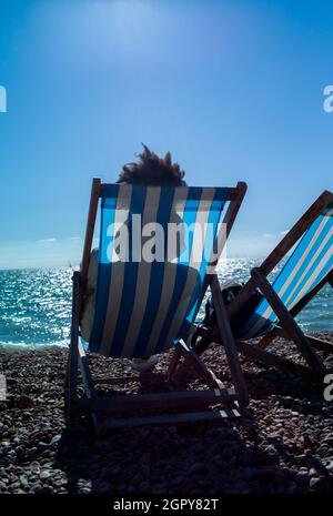 jeune femme se relaxant sur la plage dans un transat sous le soleil d'été.Sa coiffure afro est visible au-dessus de l'arrière du transat rayé Banque D'Images