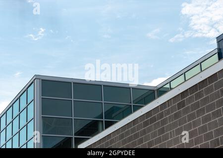 Coin extérieur d'un bâtiment avec fenêtres en verre, un mur de panneaux composites en métal bleu, une base murale en brique marron foncé avec mortier gris. Banque D'Images
