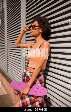 Une jeune mulatta avec une planche à roulettes dans les mains debout près du mur Banque D'Images