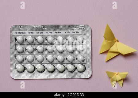 Tête d'un tableau complet des pilules contraceptives et des papillons en papier jaune origami sur fond rose Banque D'Images