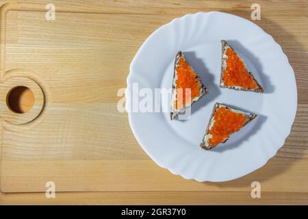 Petits sandwiches avec caviar en forme de triangle sur une plaque ronde blanche sur fond de bois. Photo de haute qualité Banque D'Images