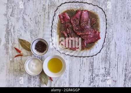 Viande crue marinée sur une assiette avec des ingrédients sur une table en bois Banque D'Images