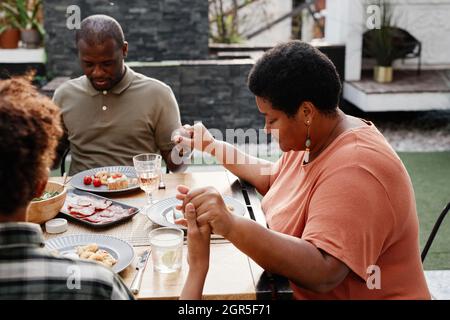 Portrait d'une femme afro-américaine senior tenant les mains avec la famille lors d'un dîner à l'extérieur et priant, espace de copie Banque D'Images
