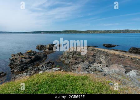 Une côte et une falaise escarpées au premier plan près d'un océan bleu profond.C'est une journée ensoleillée avec un ciel bleu et quelques nuages. Banque D'Images