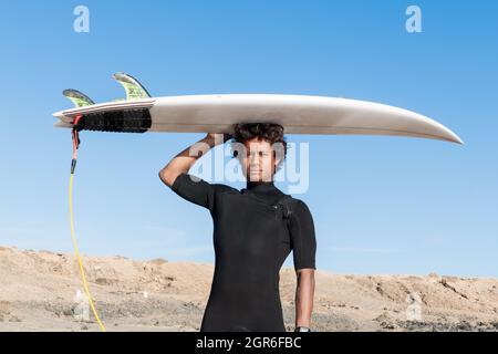 Jeune africain malgache sportif surfeur portrait tenant une shortboard portant une combinaison courte noire Banque D'Images
