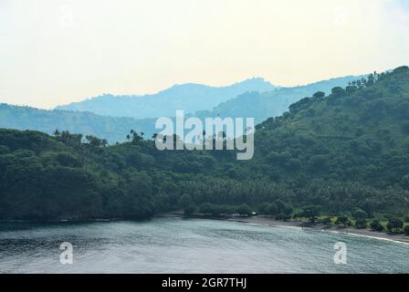 Des rangées de montagnes basses sur l'île indonésienne de Lombok, avec l'océan au premier plan, et un ciel gris clair au-dessus. Banque D'Images