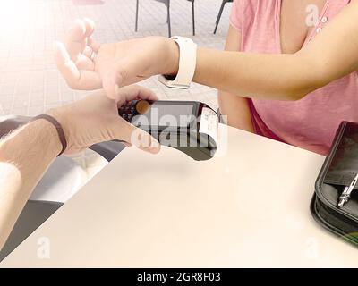 Femme caucasienne méconnaissable utilisant une montre intelligente pour payer sans fil lors d'une journée ensoleillée. Banque D'Images