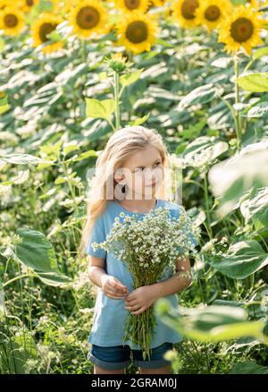 Bonne petite fille sur le champ des tournesols en été. Banque D'Images