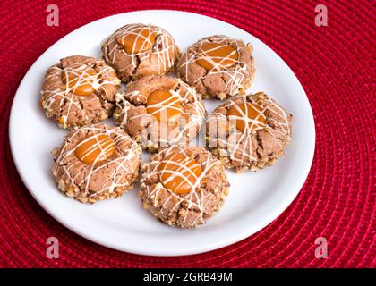 Sept biscuits bruns aux noisettes et aux cacahuètes cassants sur une assiette brune transparente, crème caramel. Plaque blanche sur fond rouge Banque D'Images